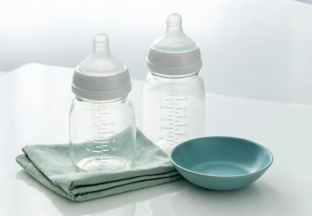 Glass baby bottles and silicone nipples arranged beside measurement notes