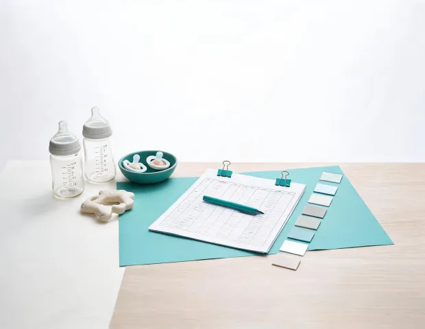 Baby feeding care product review desk with bottles, pacifiers, standards sheet, and material swatches